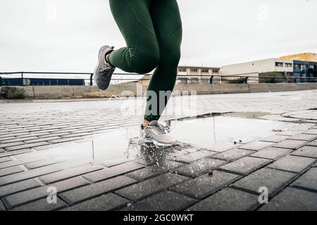 Donna non riconosciuta con abbigliamento sportivo che corre e si allena in città durante la giornata delle piogge. Foto Stock