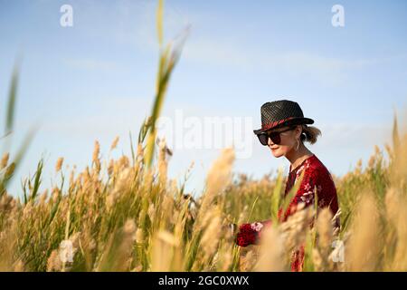 bella donna asiatica con cappello di paglia e occhiali da sole che cammina in una palude di canna Foto Stock