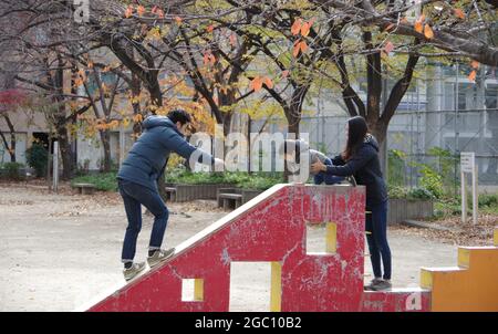 Giovane genitore giapponese che gioca con il bambino nel parco cittadino in autunno Osaka Foto Stock