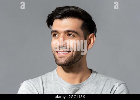 Primo piano ritratto di felice bel giovane uomo millenario caucasico guardando da parte su isolato sfondo grigio chiaro studio Foto Stock