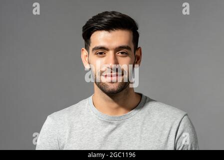 Primo piano ritratto di un bel sorriso giovane uomo caucasico volto guardando la fotocamera su uno sfondo isolato grigio chiaro studio Foto Stock
