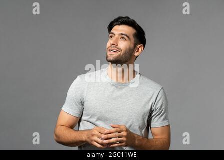 Pensando bello giovane uomo caucasico con le mani che guardano verso l'alto su sfondo grigio chiaro studio Foto Stock