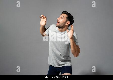 Sorpreso scioccato giovane uomo caucasico con gesti a mani aperte guardando da parte e gaping in grigio chiaro isolato sfondo studio Foto Stock