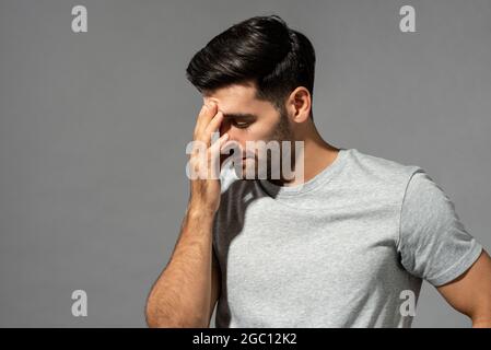 Giovane uomo caucasico che ha mal di testa e sforzo oculare, studio girato su sfondo grigio isolato Foto Stock