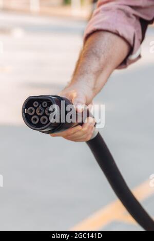 Presa per auto elettrica o EV tenuta con una mano in una stazione di ricarica. Alimentazione elettrica e concetto di energia alternativa ecocompatibile Foto Stock