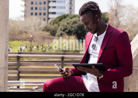 uomo d'affari nero che utilizza un tablet e uno smartphone all'aperto in città, tecnologia e concetto di lavoro remoto Foto Stock