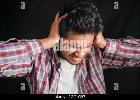 giovane uomo che ha dolore alle orecchie che tocca il suo orecchio doloroso isolato su nero Foto Stock