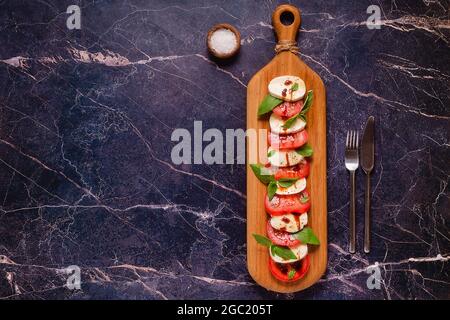Insalata caprese italiana con pomodori a fette, mozzarella, basilico, olio d'oliva su tavola di legno. Foto Stock