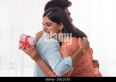 UNA GIOVANE DONNA CHE ABBRACCIA IL FRATELLO MENTRE TIENE IL REGALO Foto Stock