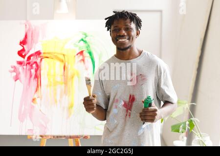 Ritratto di pittore maschile afroamericano al lavoro che tiene pennello e pittura in studio d'arte Foto Stock