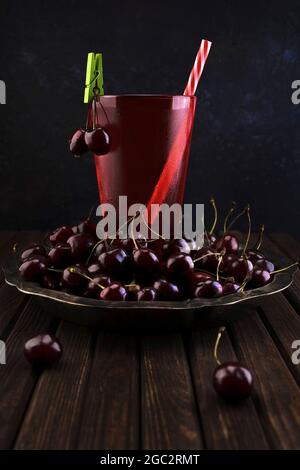 Frutta fresca biologica di amarena in un piatto d'argento vintage e un bicchiere di succo di ciliegia su un vecchio tavolo scuro fatto di tavole di legno Foto Stock