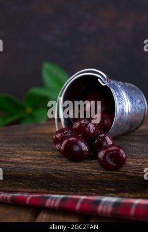 Un piccolo secchiello in alluminio con frutta fresca di ciliegia rossa organica sparsa su un vecchio pannello testurizzato in legno. Foto del cibo Foto Stock