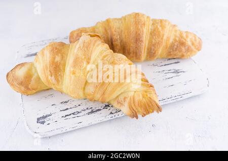 Croissant freschi su una tavola d'epoca in legno in stile provenzale su sfondo grigio chiaro Foto Stock