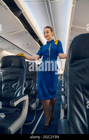 Sorridente stewardess appoggiandosi le sue mani guanto sui sedili della compagnia aerea Foto Stock