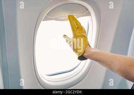 Mano con guanti che chiude le sfumature della finestra sull'aereo Foto Stock