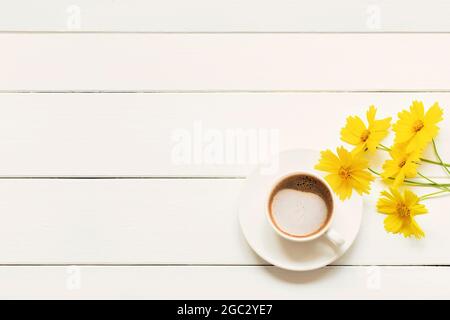 Tazza mattutina di cappuccino di caffè fresco con fiori gialli primaverili su un tavolo di legno bianco. Vista dall'alto con spazio per la copia. Foto Stock