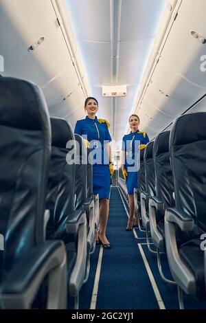 Due hostess in uniformi appoggiate sui sedili della compagnia aerea Foto Stock