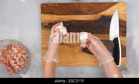 Carne di pollo tritata in una ciotola e aglio su tagliere di legno, vista dall'alto, mani donna Foto Stock