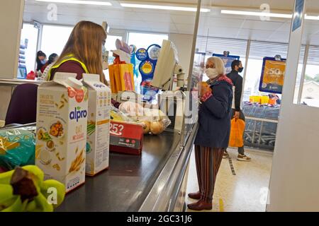 Sainsburys supermercato femmina checkout operaio acquirenti indossare maschere viso e Alpro oat drink cartoni alimentari prodotti sul banco in Galles UK KATHY DEWITT Foto Stock