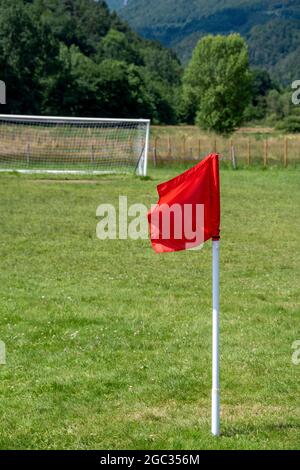 Una bandiera rossa d'angolo si erge su un lussureggiante campo da calcio verde in un tranquillo ambiente di campagna durante un pomeriggio di sole Foto Stock