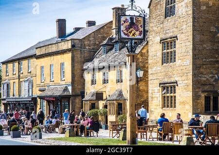 La gente gode del sole primaverile, fuori da un pub nella città di Cotswold di Broadway nel Worcestershire. Foto Stock