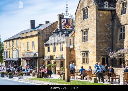 La gente gode del sole primaverile, fuori da un pub nella città di Cotswold di Broadway nel Worcestershire. Foto Stock