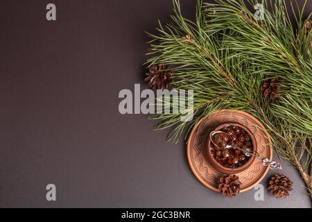Confettura di cono di pino dolce. Dessert Siberiano tradizionale, rami freschi sempreverdi. Fondo in cemento di pietra nera, vista dall'alto Foto Stock
