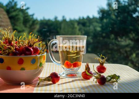 Tè alle rose e frutti di rosa selvatici in una ciotola. Visualizza dalla finestra sullo sfondo. Foto Stock