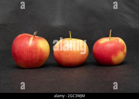 Tre mele rosse dolci biologiche fresche mature con macchie gialle, primo piano, su sfondo nero. Foto Stock