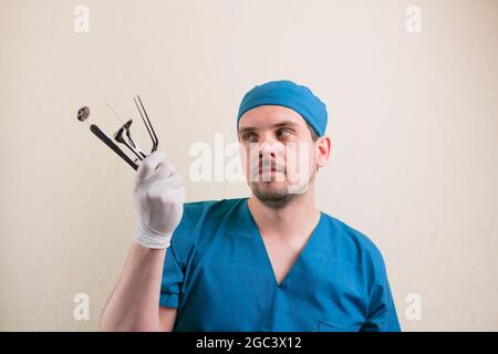 Giovane medico sorridente con strumenti medici in mano in tuta chirurgo blu isolato Foto Stock