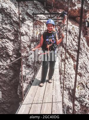 Questa giovane donna attraversa il ponte della gola sul tratto finale della Via ferrata Klettersteig Brigata Tridentina che conduce al Rifugio Pisciadu nel Gruppo del Sella, non lontano dal Passo Gardena-Groednerjoch nelle Dolomiti italiane dell'Alto Adige. Foto Stock