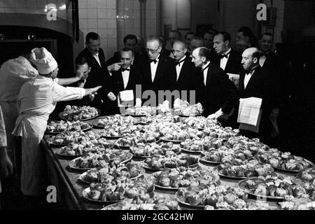 Dietro le quinte in un banchetto di stato. Banchetto di ritorno per la Regina Elisabetta II alla Mansion House, Londra dopo il suo Commonwealth Tour nel 1954. La società di catering di Ring & Brymer (Birch’s) Ltd ha gestito il catering in ogni banchetto di coronazione dato dalla Corporation of London sin dall’incoronazione della Regina Victoria e ha prestato servizio per più teste coronate di qualsiasi altra azienda al mondo. 19 Maggio 1954 Mostre fotografiche: Il piatto principale – Pollo di Primavera. Mentre i camerieri accodano, i cuochi li tengono indietro e il capo cameriere Seabanne (al centro, puntando) organizza la distribuzione Foto Stock