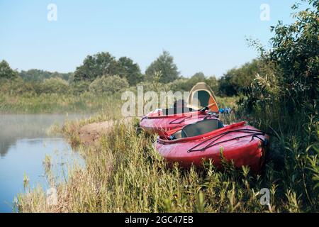 Due kayak a terra con una tenda sullo sfondo. Campo di mattina sulla riva del fiume. Foto Stock