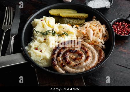 Salsiccia fritta bavarese su crauti in padella di ghisa, su vecchio sfondo di legno scuro Foto Stock