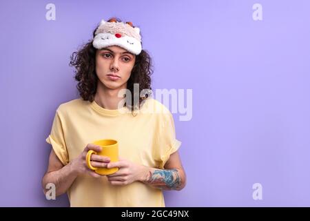 Stanco rilassato maschio non vuole andare a studiare o a lavorare, in piedi con Mug in mani guardando il lato, vuole dormire. Sfondo viola isolato Foto Stock