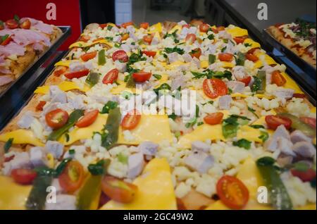 Pizza siciliana quadrata chiamata Sfinchini su un vassoio nel ristorante fast food. Pizza quadrata con pomodori ciliegini, formaggio, cetrioli e pollo. Foto Stock