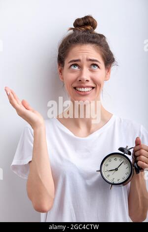 Perché dovrei svegliarmi presto la mattina... la donna è frustrato dalla sveglia, stendendo le braccia, guardando in su, vuole dormire la mattina, non ha enou Foto Stock