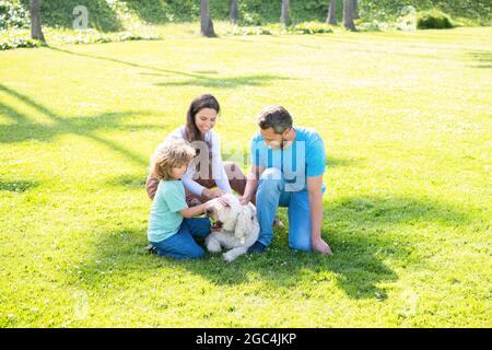 famiglia felice di papà madre e figlio bambino che gioca con cane animale domestico in erba verde parco, estate. Foto Stock