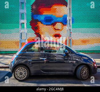 Budapest, Ungheria, marzo 2020, vista di un'auto nera Fiat 500 parcheggiata in una strada di fronte al murale colorato su un muro di mattoni Foto Stock