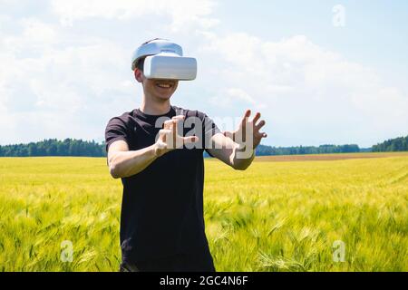 Uomo che usa occhiali di realtà virtuale all'esterno in natura su un campo di coltivazione del grano. Foto Stock