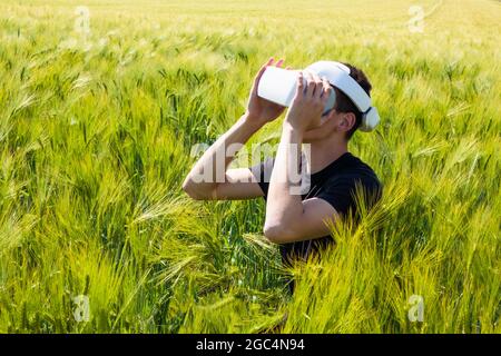 Uomo che usa occhiali di realtà virtuale all'esterno in natura su un campo di coltivazione del grano. Foto Stock