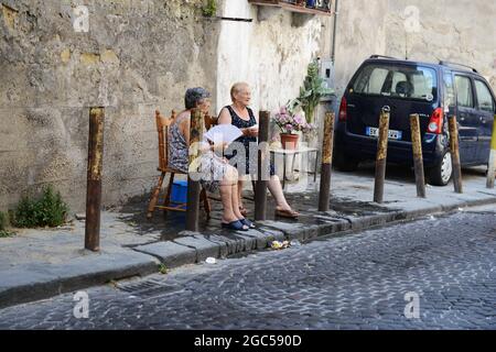 Luglio 2015, Napoli Italia. Anziane donne italiane che si siedono fuori sulla strada con un secchio d'acqua per aiutare con il calore bruciante. Foto Stock
