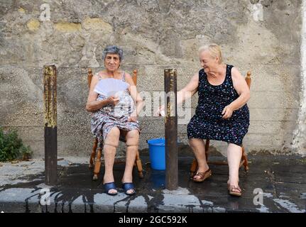 Luglio 2015, Napoli Italia. Anziane donne italiane che si siedono fuori sulla strada con un secchio d'acqua per aiutare con il calore bruciante. Foto Stock
