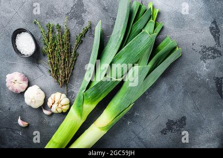 Gambi di porri con erbe ingredienti per cucinare porri brasati, su tavola grigia testurizzata vista dall'alto con spazio per il testo. Foto Stock