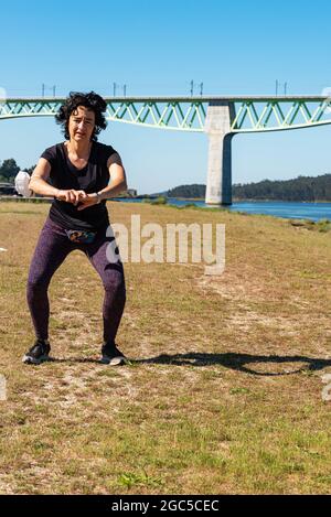 giovane donna caucasica allenare lo sport yoga sul fiume con ponte sullo sfondo Foto Stock
