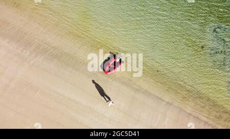 Vista aerea dell'uomo che cammina sulla spiaggia vicino al dinghy rosso. No MR o PR Foto Stock