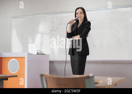 Foto ritratto di un'amica e sicura insegnante asiatica in una divisa nera da lavoro con un tablet digitale e un computer portatile per insegnare la lan moderna Foto Stock