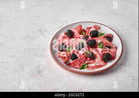 Fette di prosciutto coppa di parma con basilico e mora su piastra in ceramica su fondo testurizzato. Spazio di copia Foto Stock