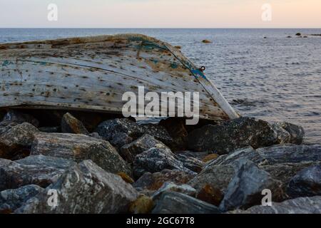 Vecchio abbandonato capovolto barca di legno di pesca in rocce sul mare Foto Stock