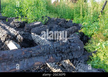 Parte di una casa di legno bruciata su uno sfondo di erba verde in una giornata estiva soleggiata. Messa a fuoco selettiva. Primo piano Foto Stock